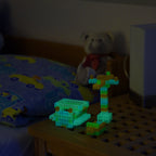 Aus Klemmbausteinen gebaute Modelle auf einem Nachttisch, im Dunkeln grünlich leuchtend
