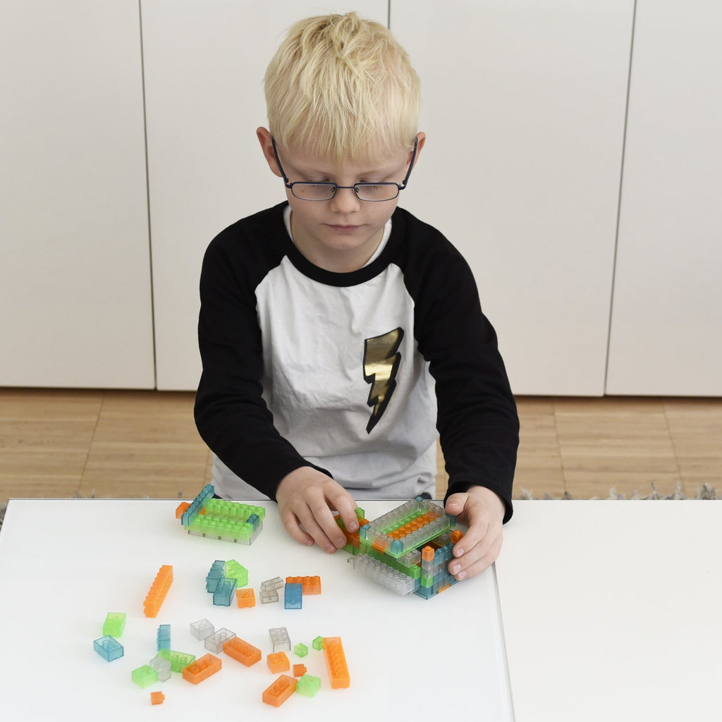 Kind baut mit bunten transparenten Klemmbausteinen an einem weißen Tisch