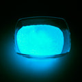 Leuchtgranulat Blau 1 mm in einer Glasschale im Dunkeln, blau leuchtend