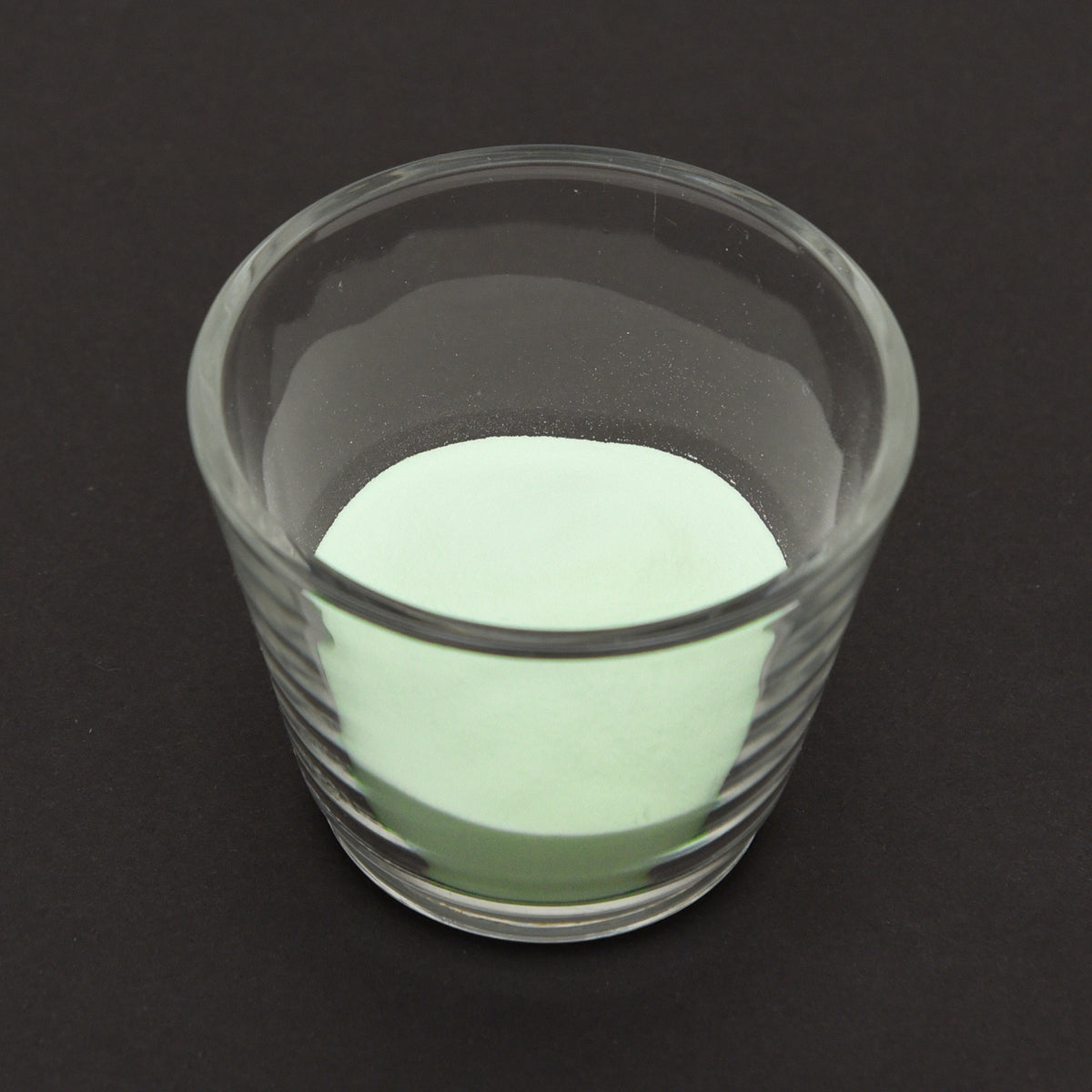 Leuchtgranulat Blau 1 mm in einem Glas bei Tageslicht, blassgrün