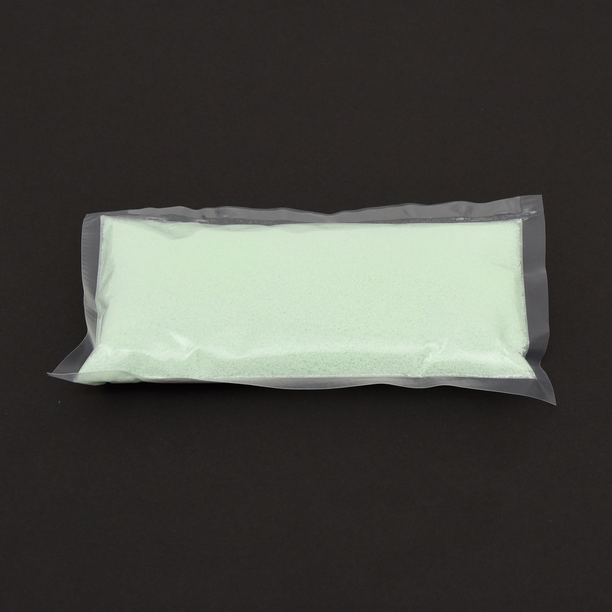 Leuchtgranulat Blau 1 mm im durchsichtigen Beutel, blassgrünes Granulat auf dunklem Grund