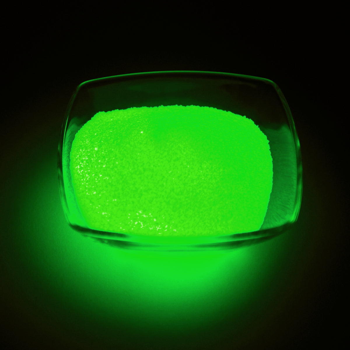 Leuchtgranulat Grün 1 mm, 100 g in einer Glasschale, im Dunkeln grün leuchtend