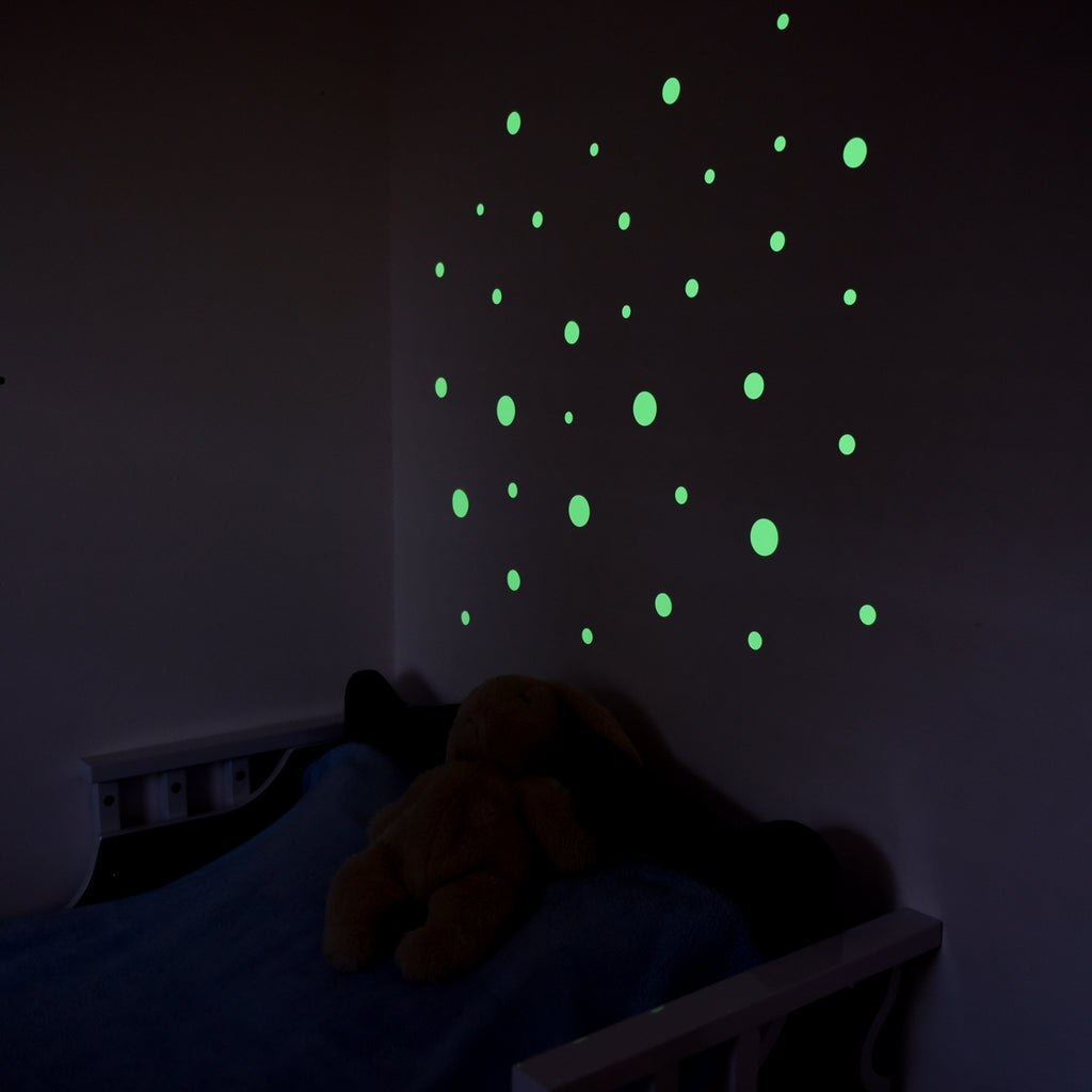 Leuchtpunkte an der Kinderzimmerwand im Dunkeln, darunter Bett mit Stofftier