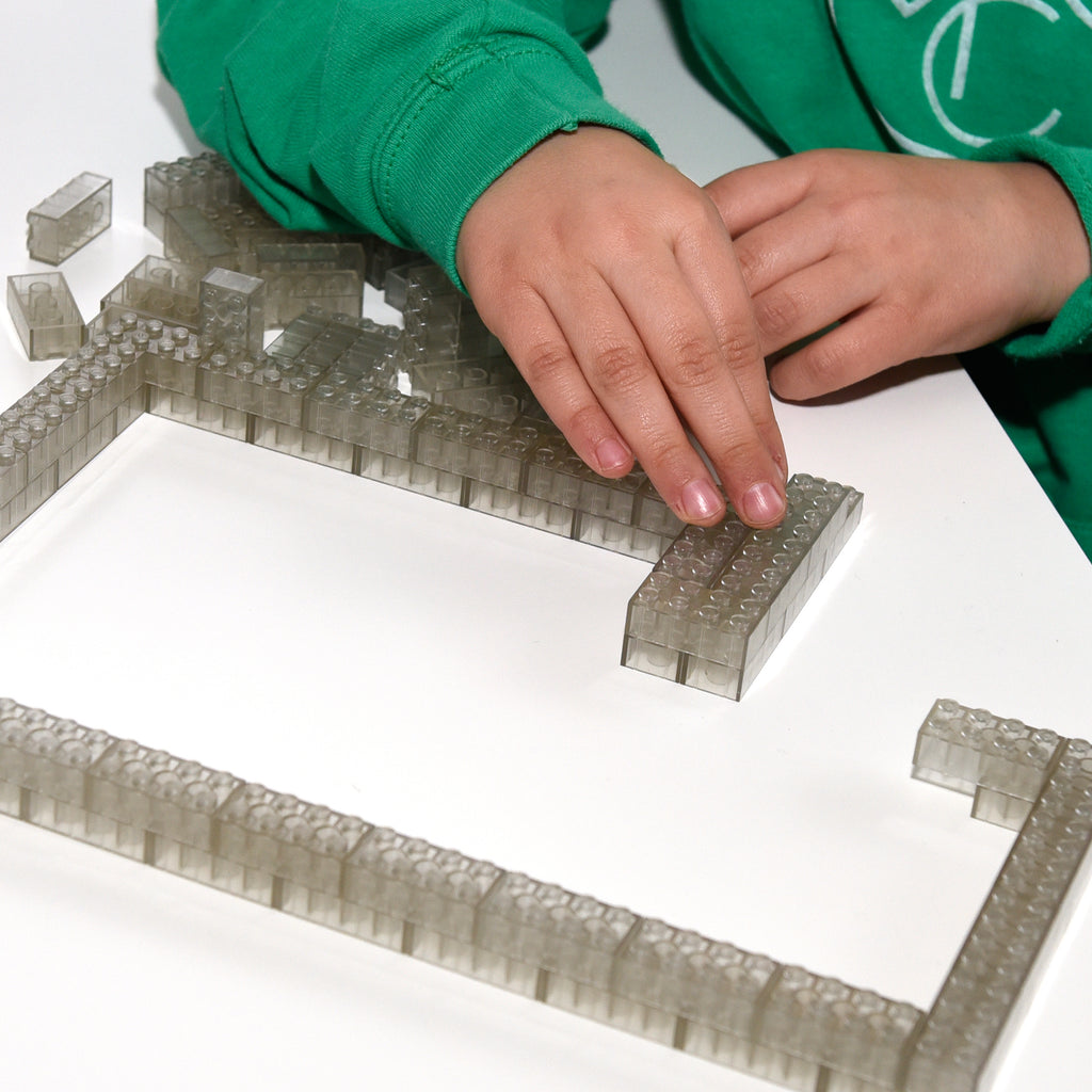 Transparente Klemmbausteine 2x4 bei Tageslicht, Kinderhand baut eine Wand