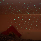Leuchtsterne an der Zimmerdecke und Wand eines Kinderzimmers im Halbdunkel, Teddy auf dem Bett