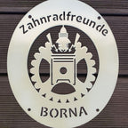 Vereinswappen aus Metall mit Pulverlack beschichtet bei Tageslicht, helles Schild an Holzwand
