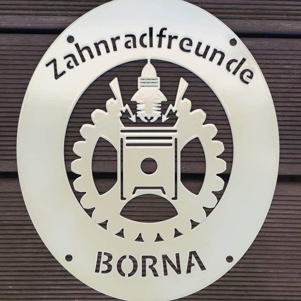 Vereinswappen aus Metall mit Pulverlack beschichtet bei Tageslicht, helles Schild an Holzwand